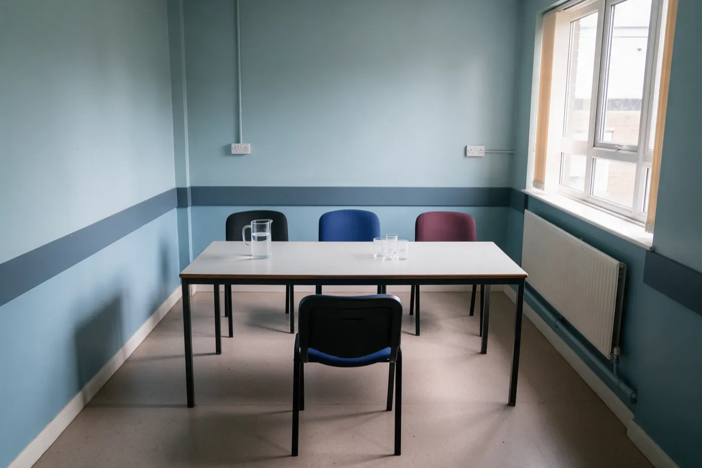 A hospital meeting room set for an interview: three chairs behind a table facing one empty chair